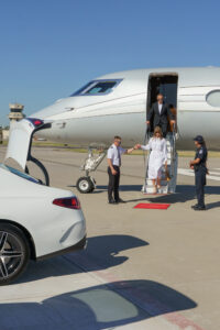luxury fbo dallas- a pilot in uniform helping a woman walk down the steps from the jet onto the tarmac. a man walks behind